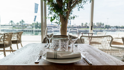 Table prepared on a restaurant sunny outdoor terrace with plates, wine cups, glasses and cutlery and garnished with plants