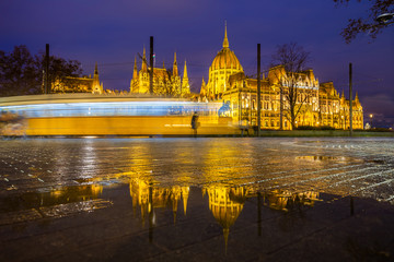 Budapest, Hungary - Illuminated Parliament of Hungary at blue hour with reflection and traditional yellow tram on the move