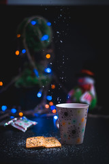 taza de café con galletas y luces decorativas en el fondo