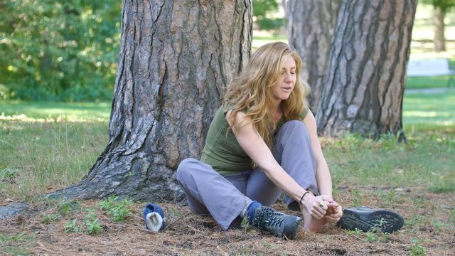 Female hiker takes off hiking sock and boot and massages sore foot.