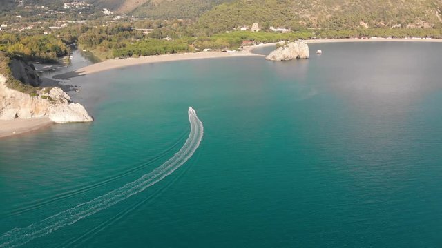 Motor boat floats towards river mouth at woody coastline. Aerial shot of sea shore. Campania, Italy