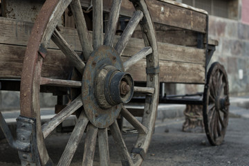 Fototapeta na wymiar Rusty metal wheel of old wooden cart. Abandoned horse wagon, traditional western films transportation