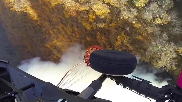 Fire fighting helicopter flying above the trees dropping water to fight the fires in California