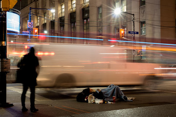 Editorial photo; Toronto, Ontario / Canada - November 13 2018: Homeless man on the streets of Toronto on a cold night with moving people and cars showing poverty in the city