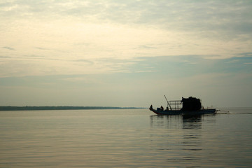 Fototapeta na wymiar A fishing boat is silhouetted against the still, calm waters of Tonle Sap lake, in the village of Kampong Khleang near Siem Reap in Cambodia