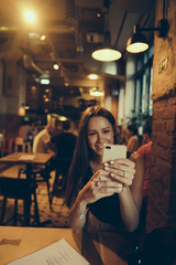 Hipster girl is holding mobile phone in hands during rest in cafe