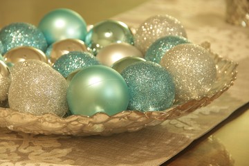Close up of Christmas ornaments in a silver textured bowl on a white lace table runner