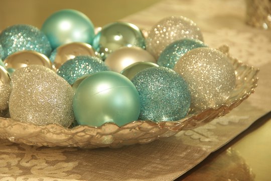 Close Up Of Christmas Ornaments In A Silver Textured Bowl On A White Lace Table Runner