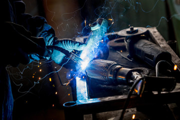 Male worker wearing protective gloves while repairing car exhaust pipe with welding machine