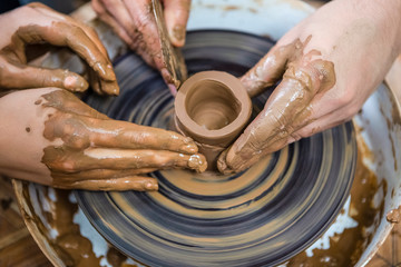 Closeup of Hands of  Male Potter Teaching His Female Apprentice to Work with Clay Lump on Potter's Wheel in Workshop.