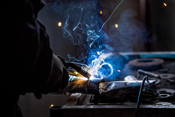 Male worker wearing protective gloves while repairing car exhaust pipe with welding machine