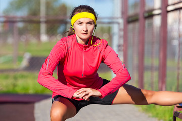 Sport Concepts. Portrait of Concentrated Caucasian Sportswoman in Outdoor Sport Outfit Having Leg Muscles Stretchings With Folded hands. Listening to Music in Headphones.