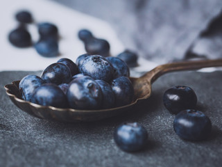 Blueberries on a spoon on slate, with slate grey linnen on white canvas background