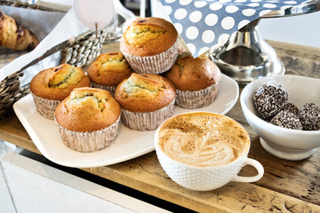 A cup of cappuccino with a plate with muffins and a white pot with truffes chocolat.