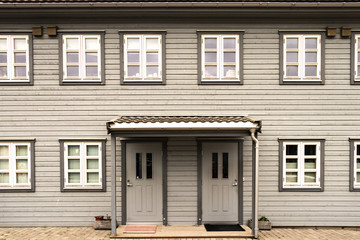 A grey wooden pattern wall with windows and two doors of a house in Norway.