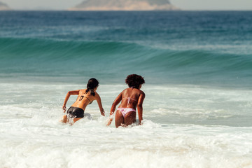 Fototapeta na wymiar Two young women, one Caucasian and one African, jump on the sea break