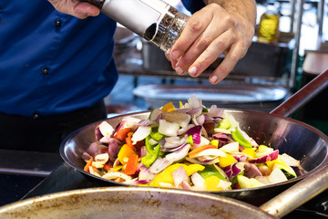 Adding the spices to the vegetables cooking in the frying pan.