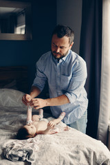 Middle age Caucasian father changing diaper for newborn baby daughter. Male man parent taking care...