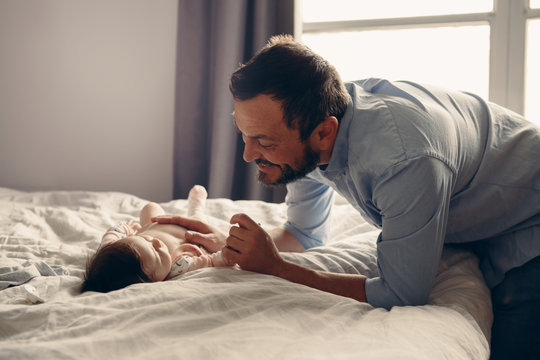 Portrait of middle age Caucasian father talking to newborn baby son daughter. Male man parent smiling to child on bed in bedroom at home. Authentic lifestyle real candid moment.