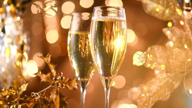 Christmas scene. Flute with sparkling champagne over holiday golden bokeh blinking background. Celebrating. 4K UHD video footage. Slow motion 3840X2160