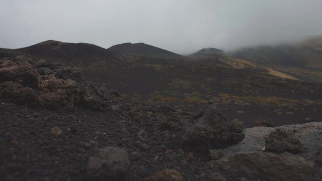 Black stones on lifless volcano slopes. Low gray clouds covere mountain top