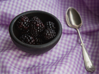 Blackberries in cast iron bowl with spoon on purple gingham