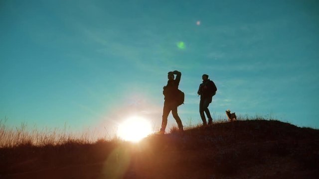 teamwork. Two hikers enjoying sunrise walking from top of a mountain and dog. Two hikers with backpacks climbing a peak on cloud sky background and dog. hikers adventure and the dog go walking. travel