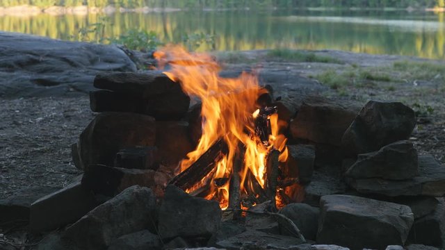 Campfire at campsite. Defocused lake and trees in the background. Summer camping at Massassauga Provincial Park, Ontario, Canada.