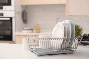 Dish drainer with clean dinnerware on table in kitchen