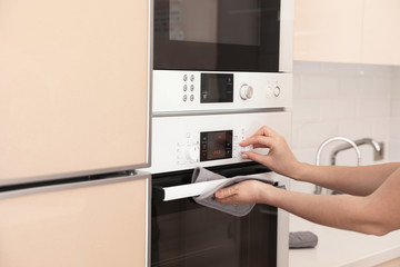 Woman adjusting electric oven in kitchen, closeup