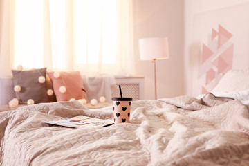 Cup of hot drink with magazines on bed at home