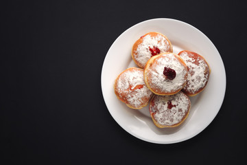 Tradition Jewish holiday sweets, donut sufganioyt with sugar powder and jam on black background top view with copy space.