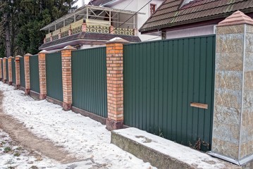 a long fence of green metal and bricks outside in the snow