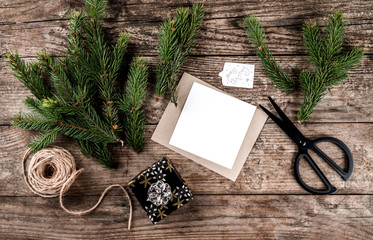 Christmas fir branches, paper card note, scissors and skein of jute on wooden background for decorated Christmas card. Xmas and Happy New Year theme. Flat lay, top view