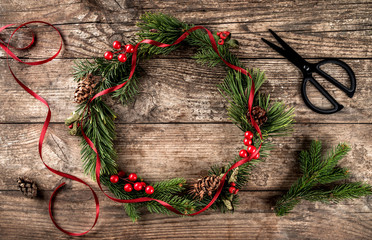 Christmas wreath of Fir branches, cones, scissors and skein of jute on dark wooden background. Xmas and Happy New Year theme, snowflakes. Flat lay, top view