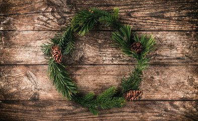 Christmas wreath of Fir branches, cones, red decoration on wooden background with snowflakes. Xmas and Happy New Year theme. Flat lay, top view