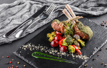Tomahawk rib beef steak on bone and vegetables with sauce on black shale board over black stone background. Hot Meat Dishes