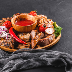 Assorted delicious grilled meat and sausages with tomatoes and bbq sauce on cutting board over black stone background. Hot Meat Dishes. Top view, flat lay