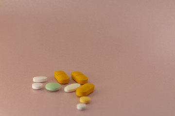 Medicines of different sizes and colors on a neutral pink background.
