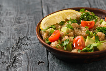 Salad of amaranth, avocado, pepper, lemon and parsley seeds with olive oil on a black wooden table.