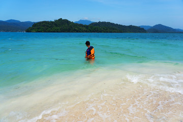 Asian young man wearing life vest standing in turquoise sea