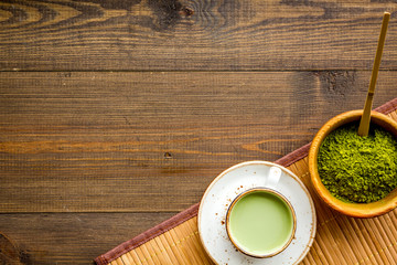 Coffee and cocktails with matcha concept. Matcha latte near bowl with matcha powder and accessories on dark wooden background top view copy space