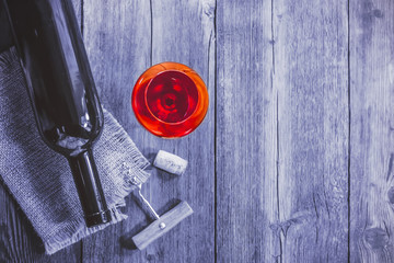 A glass of red wine on a wooden toned background with a bottle and a corkscrew.