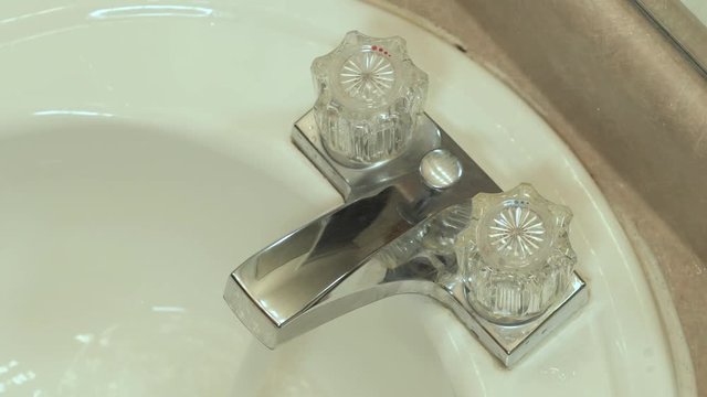 A man's hand turns on and off the hot water on a bathroom sink faucet.