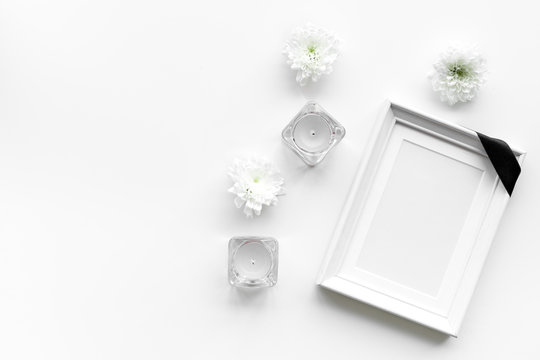 Death concept. Photo frame, mockup with black ribbon near flowers, candles on white background top view copy space