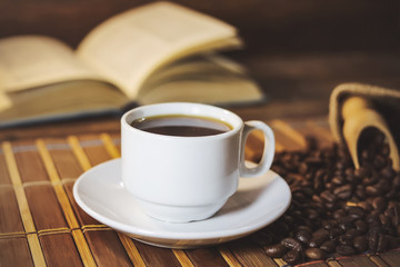 A cup of black coffee on the background of an open book. on a wooden table