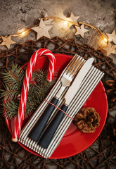 Christmas set. Red plate with cutlery with decorations on stone background.

