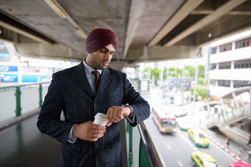 Indian Sikh businessman checking smart watch and holding coffee