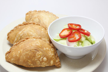 Curry puff in a dish serve with spicy sour cucumber isolated on white background, close up view.