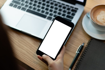 close-up on hand holding phone showing white screen on desk at coffee shop.